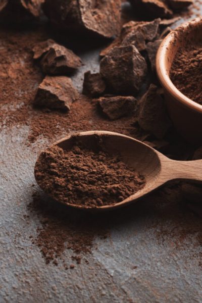 Dark chocolate pieces crushed on dark background and cocoa powder closeup, copy space. Sweet wallpaper, confectionery shop advertising and cooking ingredients concept